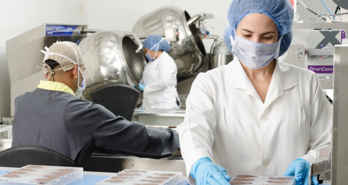 three people inside factory wearing masks and coats